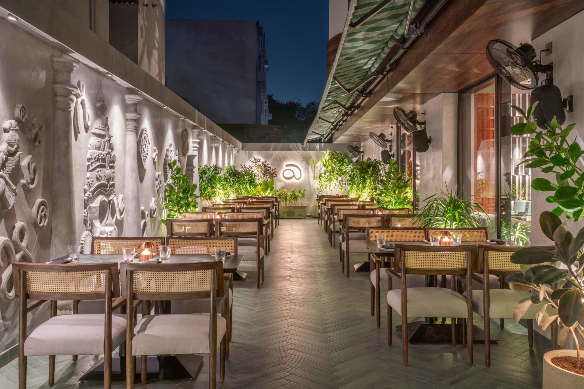 Night courtyard with cane chairs, plants and lit Aidu logo